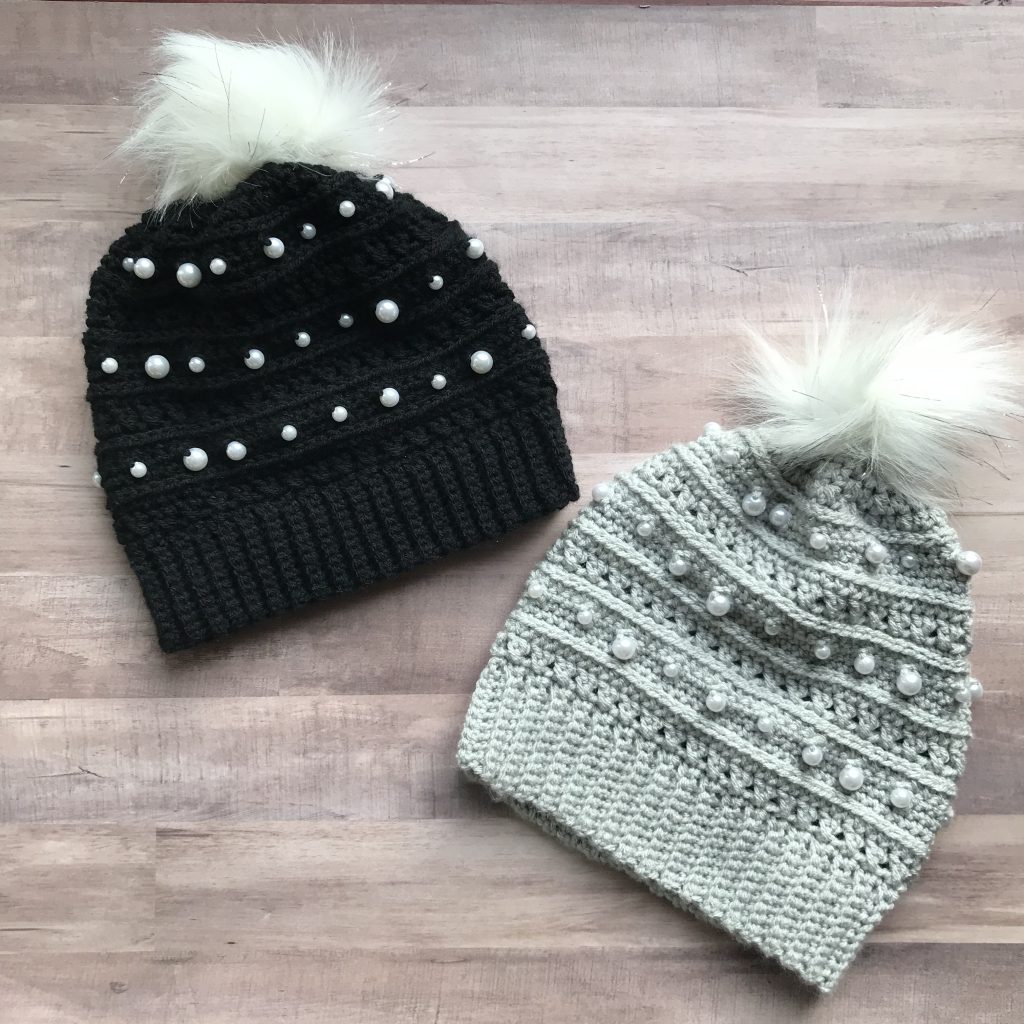 overhead view of black beaded beanie and gray beaded beanie with white faux fur poms