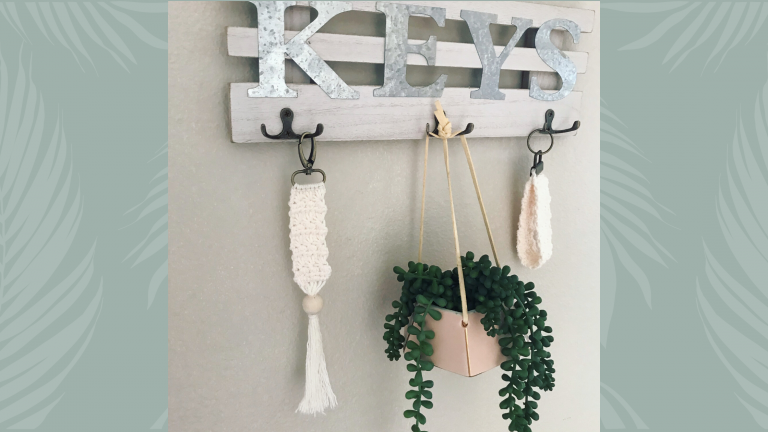 two cream keychains hanging on a key rack with small plant
