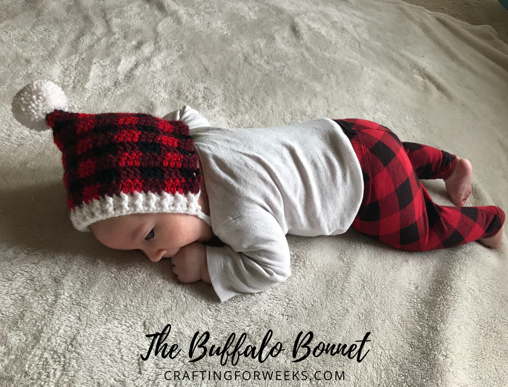 baby laying on rug wearing buffalo plaid pixie bonnet