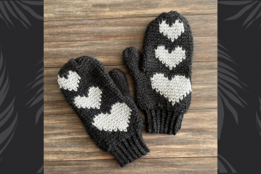 black crochet mittens with silver hearts on wood background