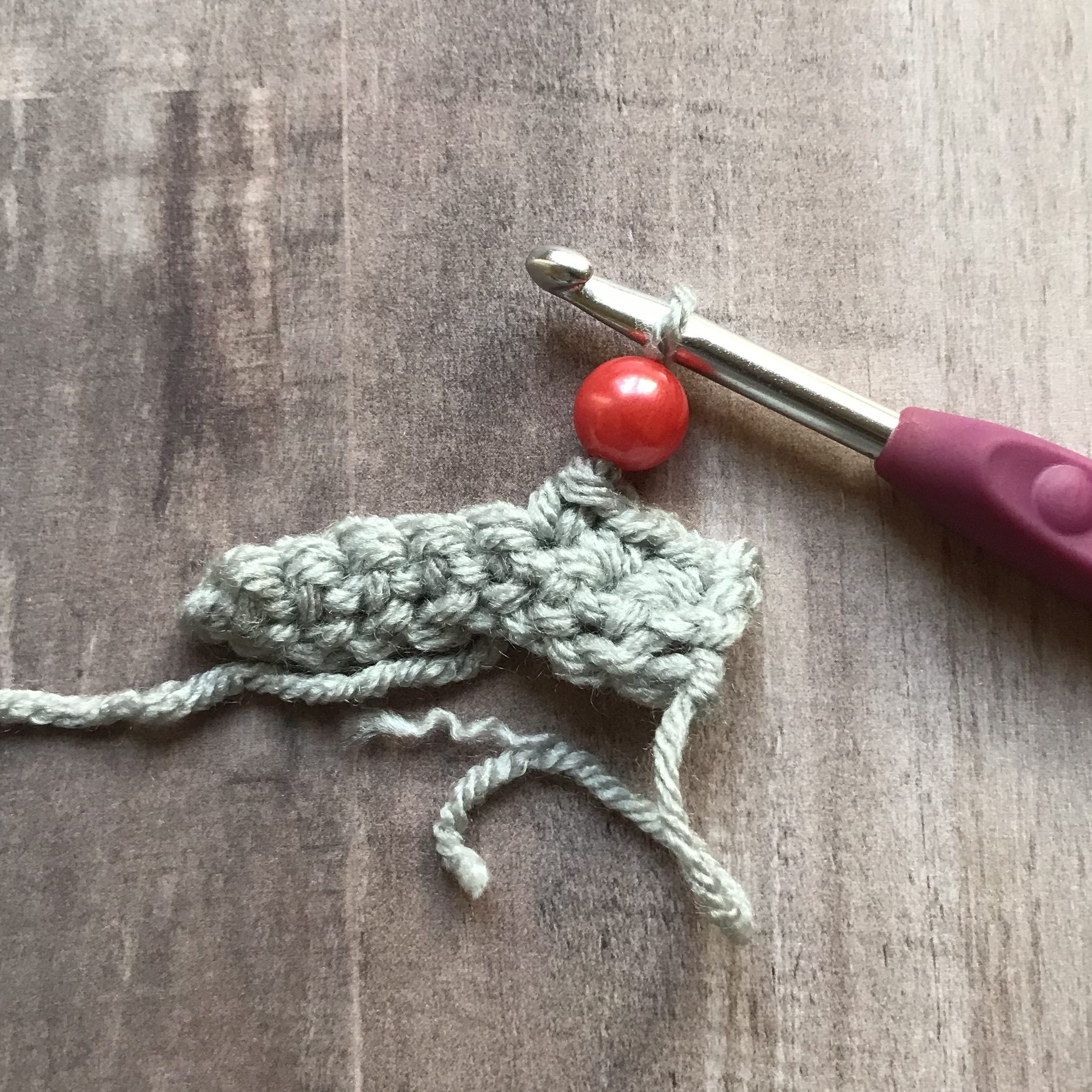 closeup of crochet hook with bead on crochet fabric