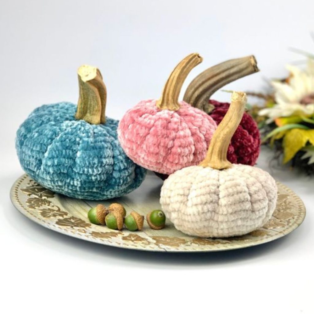 pastel colored velvet crochet pumkins with real pumpkin stems on top of a decorative cream and gold plate