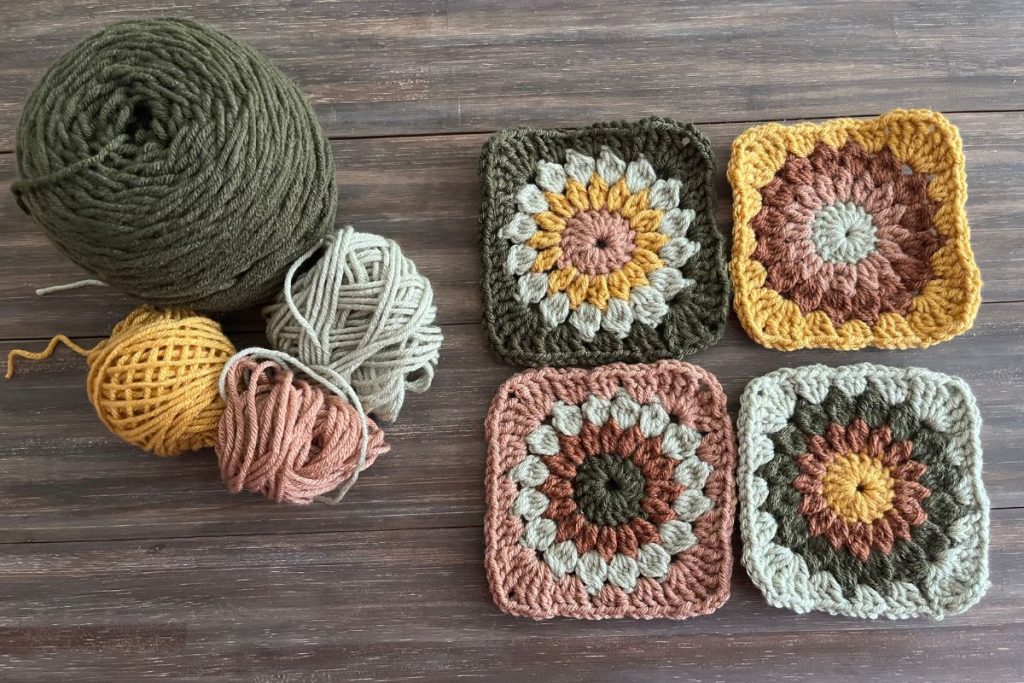 four balls of yarn in olive, mustard, sage, and tan next to four granny squares using the same colors